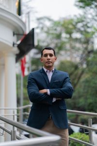 A confident man in a blazer poses outdoors, exuding professionalism and elegance.