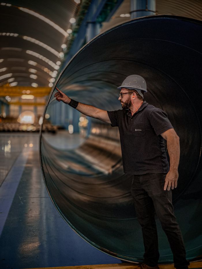 Services Engineer in helmet assessing a large pipe in a manufacturing warehouse, showcasing industrial productivity.