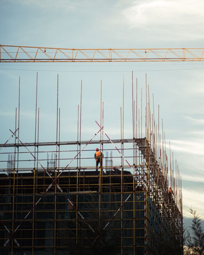 Services Scaffold workers in safety gear working on a building at sunset with clear sky.